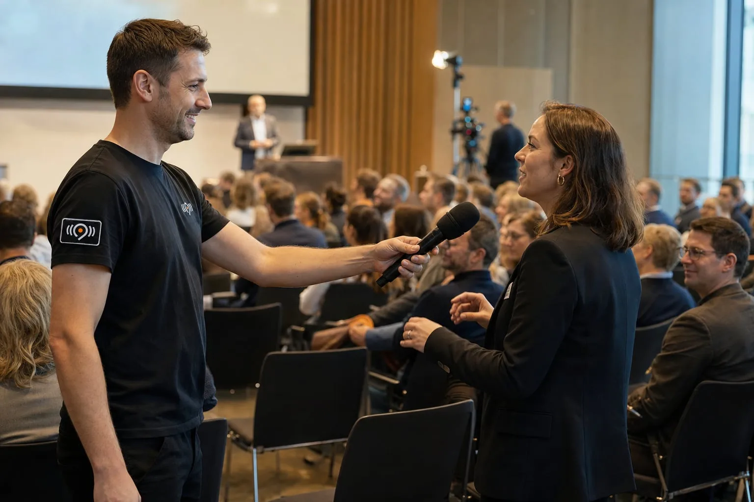 Fragerunde bei einer Konferenz: Ein Techniker hält einer Teilnehmerin das Funkmikrofon hin